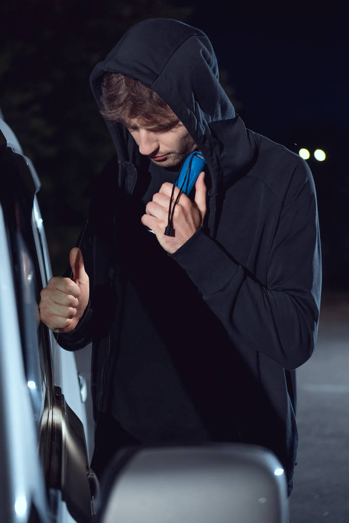 el feneri ve levye ile hoodie davetsiz arabada hırsız - Fotoğraf, Görsel