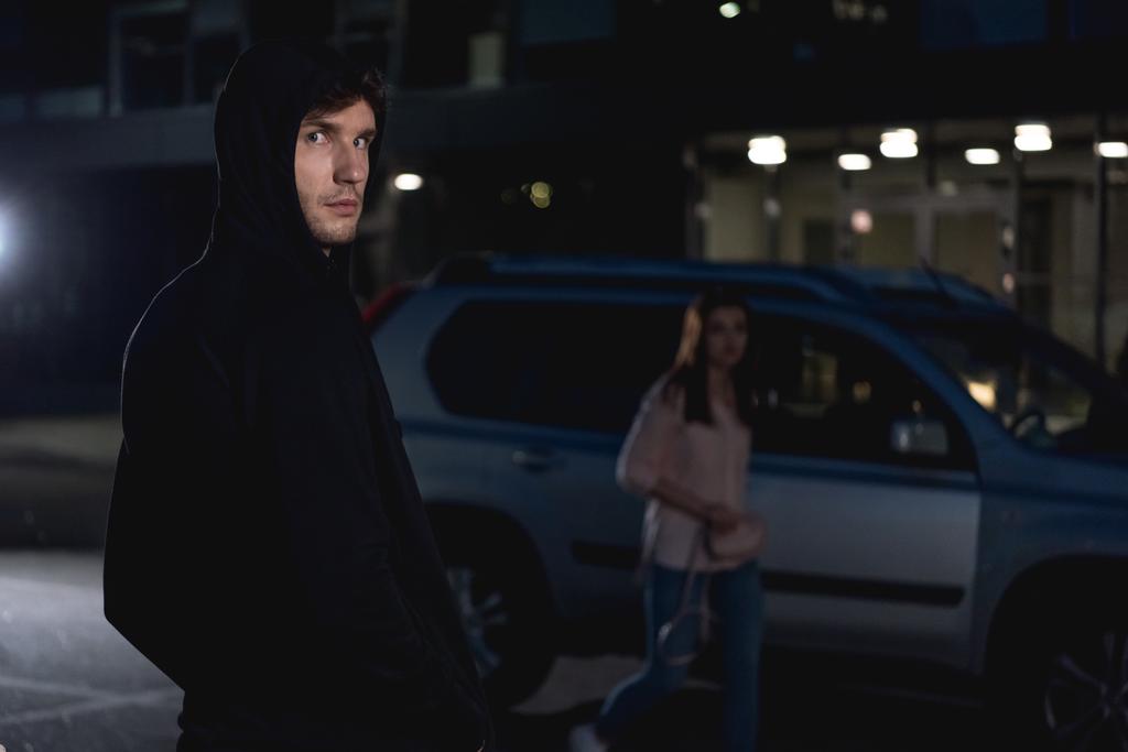 selective focus of thief looking at camera near woman walking at nighttime - Photo, Image