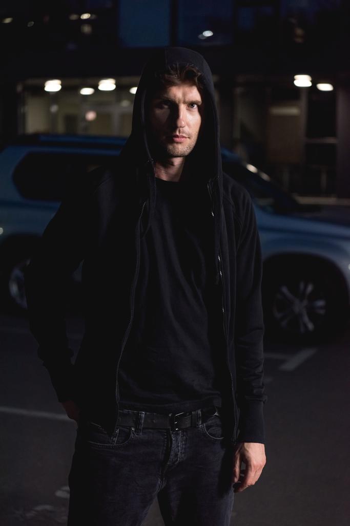 ladrão com capuz preto olhando para a câmera no estacionamento à noite
 - Foto, Imagem