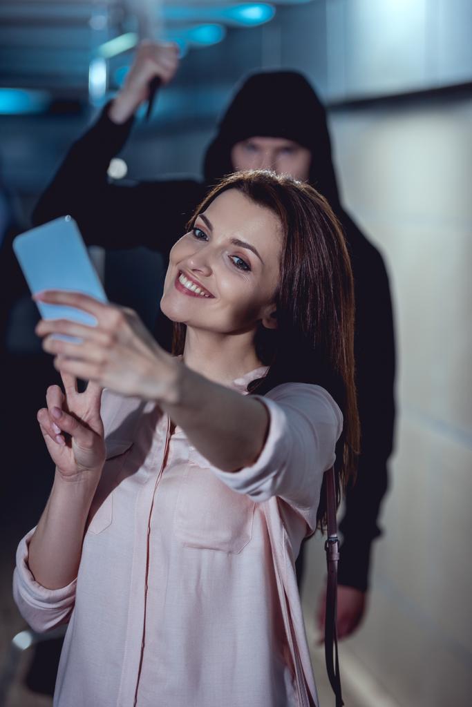 ladrão com faca atacando sorridente mulher tomando selfie no smartphone
 - Foto, Imagem