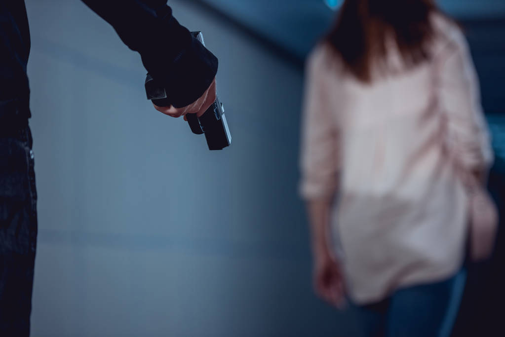 επιλεκτική εστίαση του ληστή που κρατάει όπλο κοντά στη γυναίκα - Φωτογραφία, εικόνα