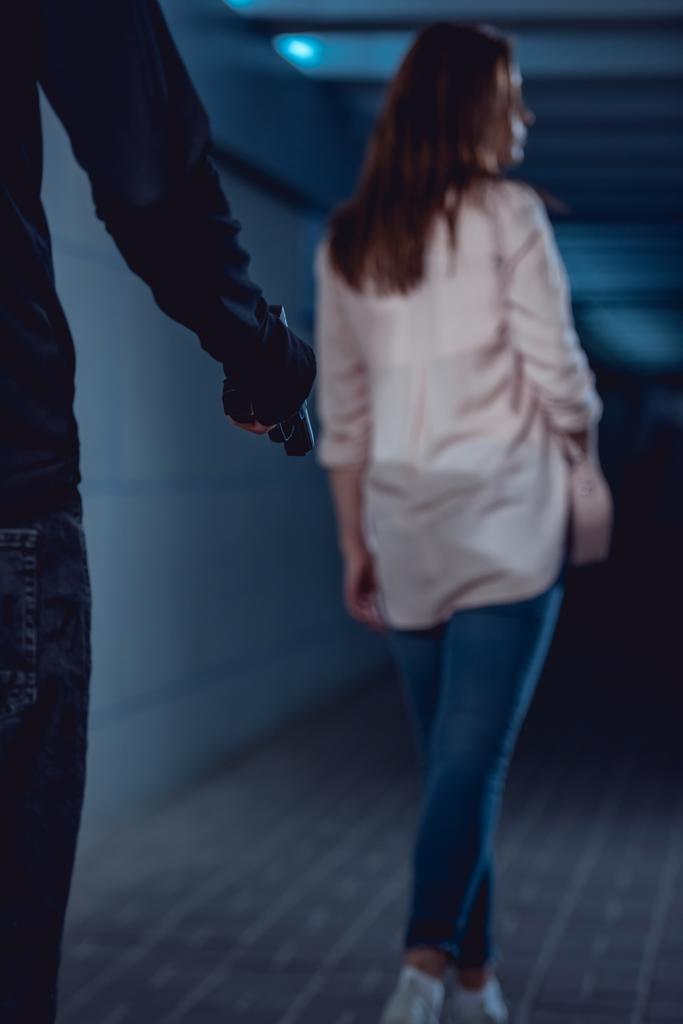 ladrón sosteniendo arma detrás caminando mujer en underpass
 - Foto, imagen