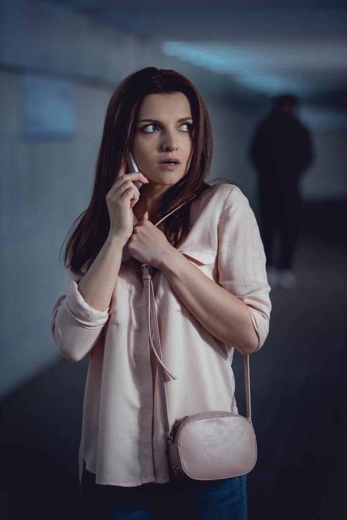 地下道で泥棒の近くでスマートフォンで話すストレスの女性の選択的な焦点 - 写真・画像