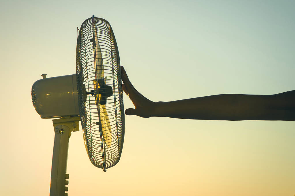 Female hand during hot weather in front of fan on a sunset sky background  - Photo, Image