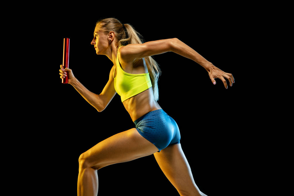 Professional female relay racer training on black studio background in neon light - Photo, Image