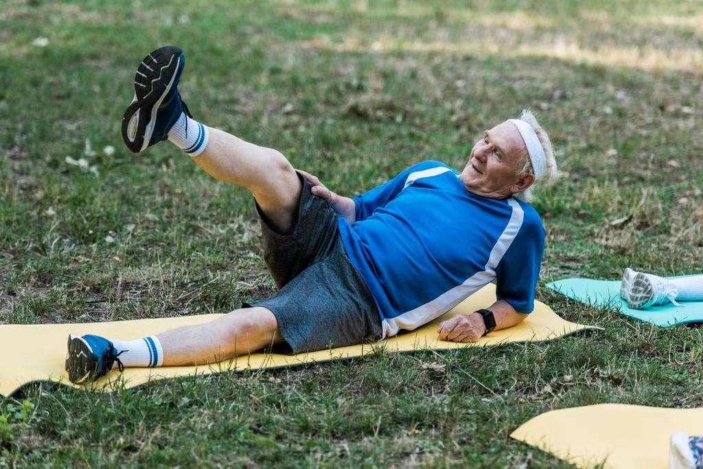Senior mit grauen Haaren trainiert auf Fintess-Matte im Park  - Foto, Bild