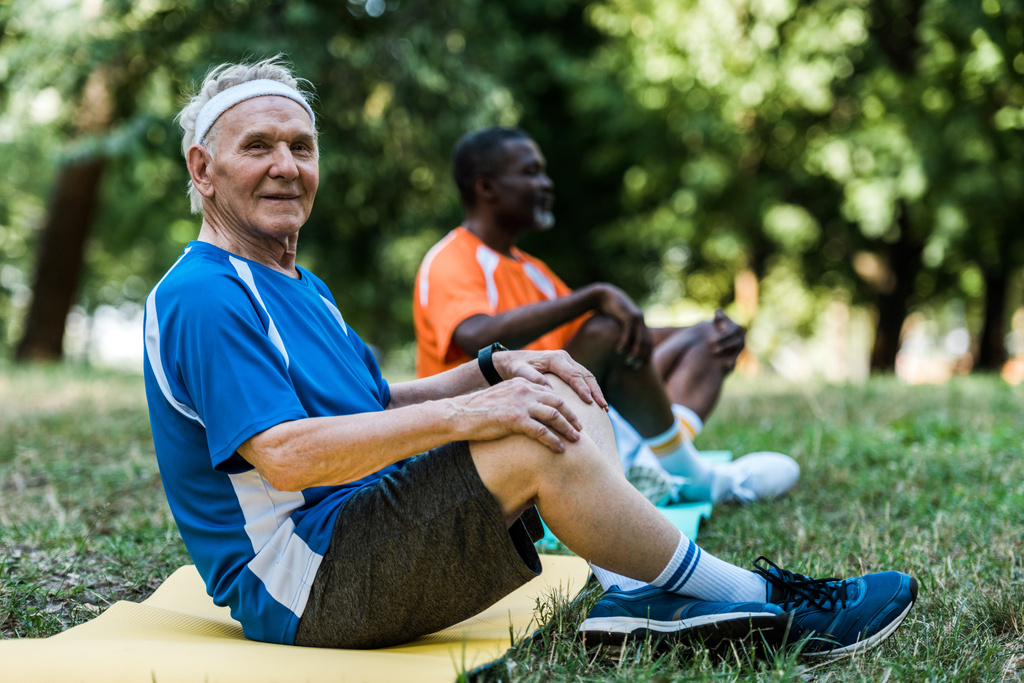selective focus of happy retired man sitting on yoga mat near african american man  - Photo, Image