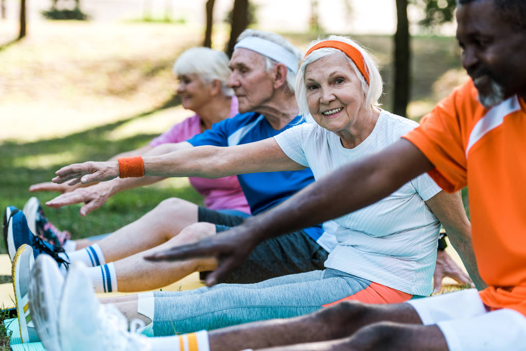 selective focus of multicultural retired women and men in sportswear exercising on fitness mats  - Photo, Image