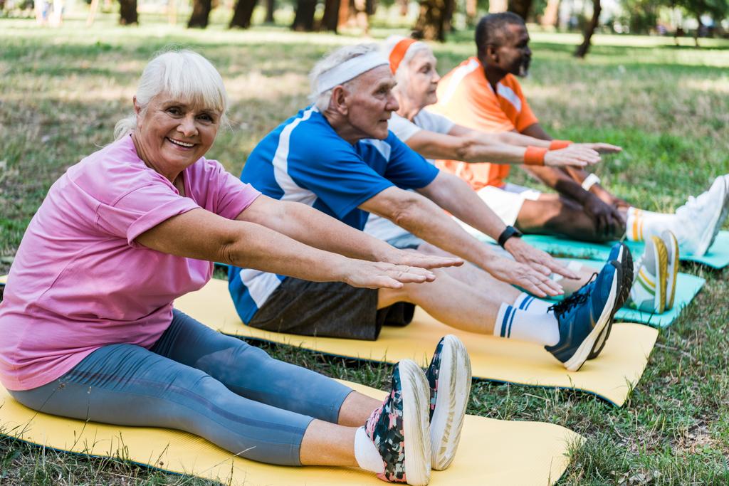 selective focus of happy senior woman in sportswear exercising  near multicultural pensioners on fitness mats  - Photo, Image