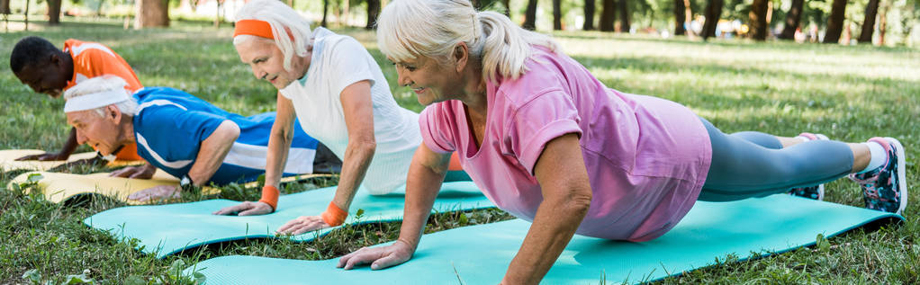 panoramic shot of sportive retired and multicultural men and woman in sportswear exercising on fitness mats  - Photo, Image