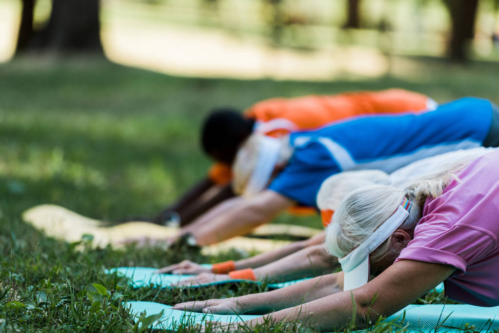 selectieve focus van multiculturele gepensioneerde vrouwen en mannen die zich uitstrekken over fitness matten in Park  - Foto, afbeelding