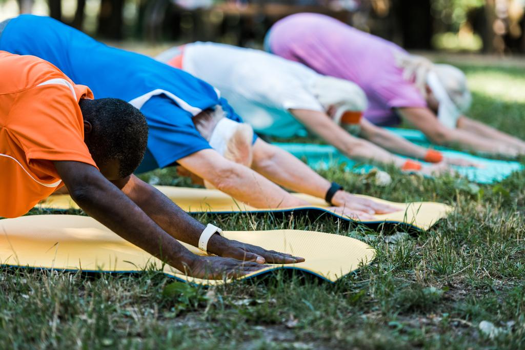 selective focus of multicultural pensioners stretching on fitness mats in park  - Photo, Image