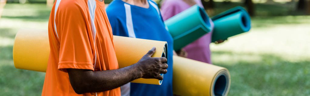 tiro panorâmico de idosos e multiculturais pensionistas segurando tapetes de fitness
 - Foto, Imagem