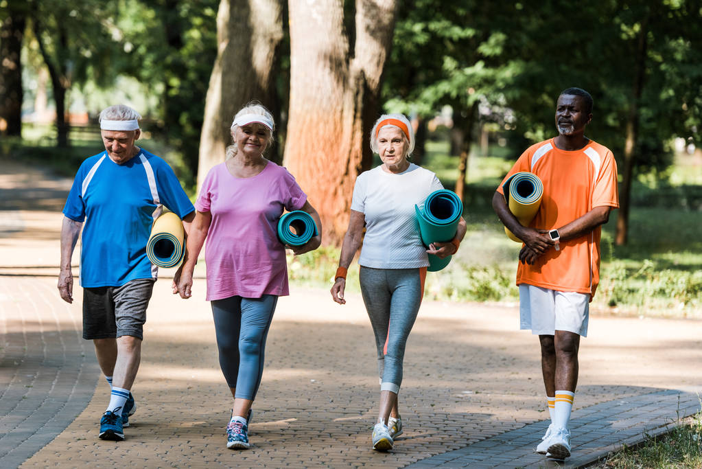 šťastní senioři a multikulturní penzisté, kteří mají fitness rohože a procházky v parku  - Fotografie, Obrázek