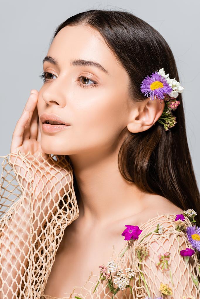beautiful model in mesh beige clothing with purple flowers touching face isolated on grey - Photo, Image