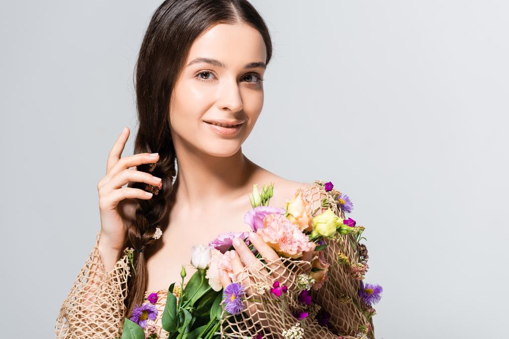 smiling beautiful woman with braid in mesh with spring wildflowers isolated on grey - Photo, Image