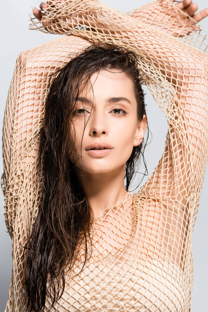 beautiful young woman with wet hair in mesh beige clothing posing isolated on grey - Photo, Image