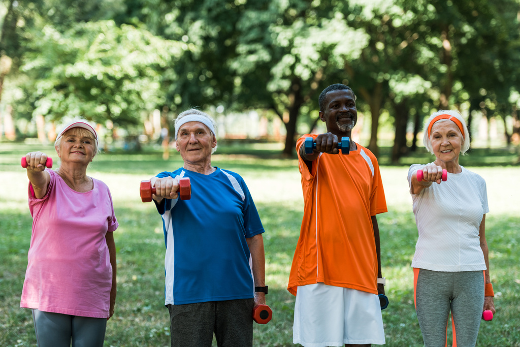 jubilados multiculturales sonrientes haciendo ejercicio con mancuernas en el parque
  - Foto, imagen