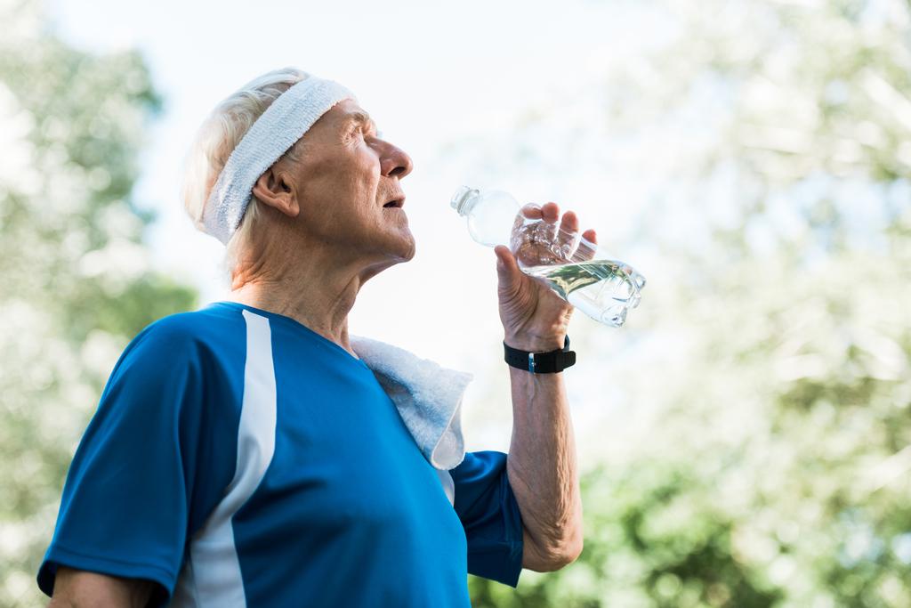 vista angolo basso dell'uomo anziano che tiene bottiglia con acqua
  - Foto, immagini