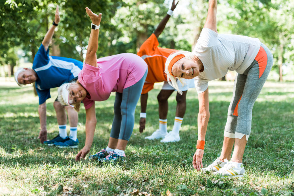 enfoque selectivo de personas mayores felices y multiculturales haciendo ejercicio de estiramiento en la hierba
  - Foto, imagen
