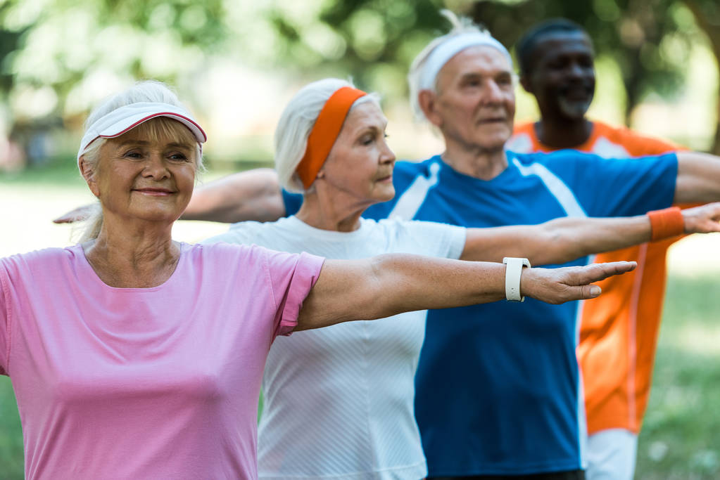 вибірковий фокус щасливої пенсіонерки, що стоїть з простягнутими руками біля мультикультурних пенсіонерів
  - Фото, зображення