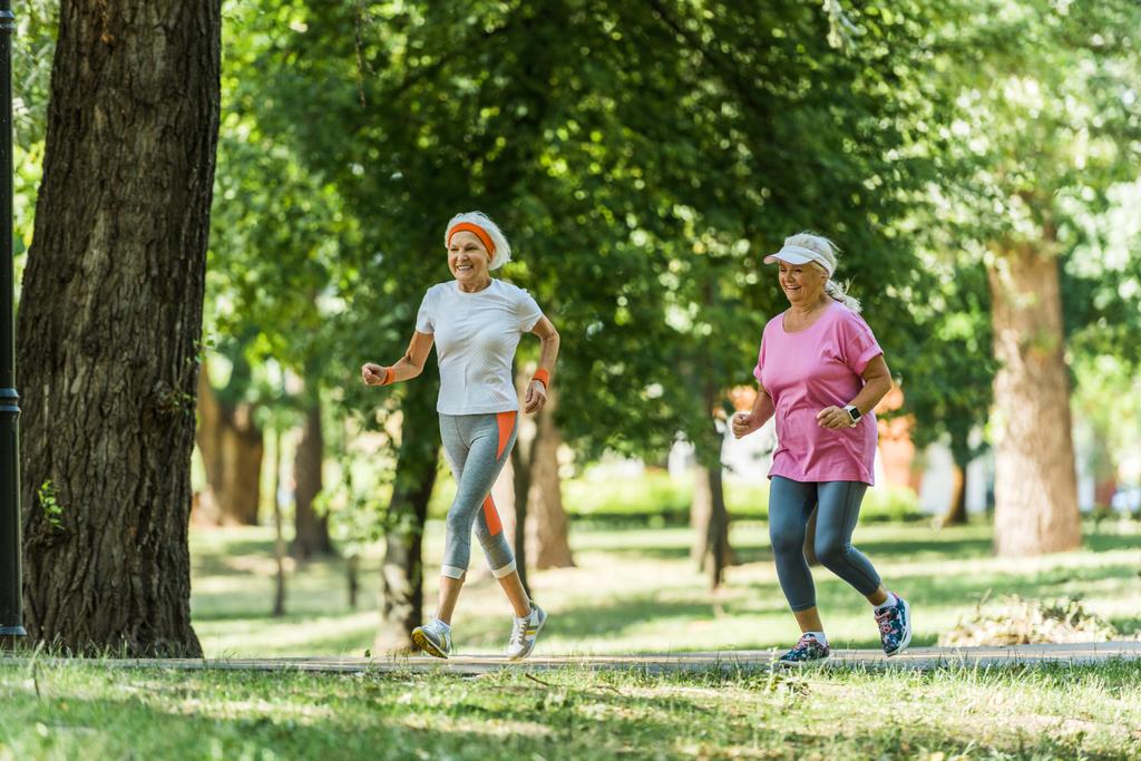 selective focus cheerful senior women in sportswear jogging in park  - Photo, Image