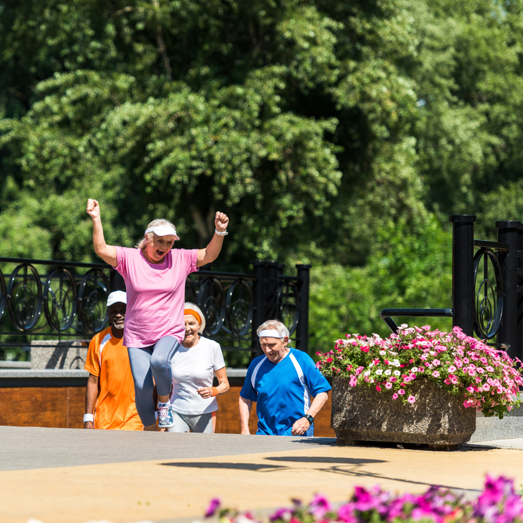selective focus of cheerful retired woman celebrating triumph near multicultural pensioners in park  - Photo, Image