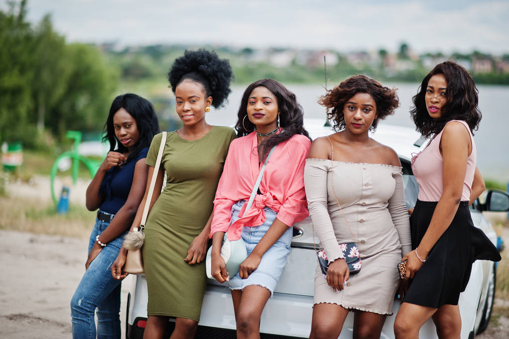 Grupa pięciu szczęśliwych afrykańskich amerykańskich dziewcząt stwarzanych przeciwko samochodom. - Zdjęcie, obraz