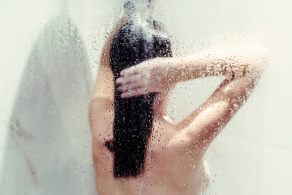 Silhouette einer nackten schönen Frau beim Haarewaschen in der Dusche hinter nassem, vernebeltem Glas. - Foto, Bild
