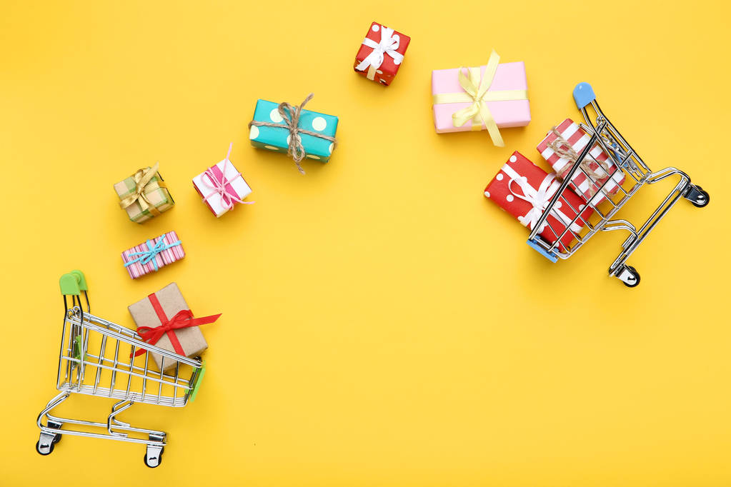 Piccoli carrelli della spesa con scatole regalo su sfondo giallo
 - Foto, immagini