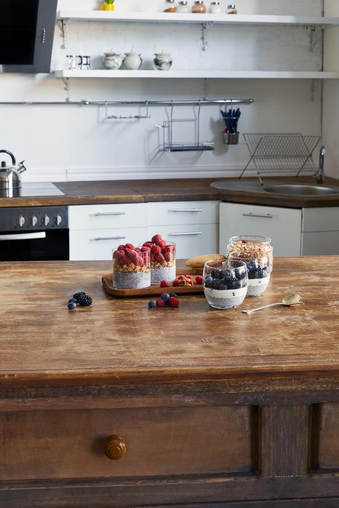 yogur sabroso con semillas de chía y bayas en vasos en bandeja de madera en la cocina
  - Foto, imagen