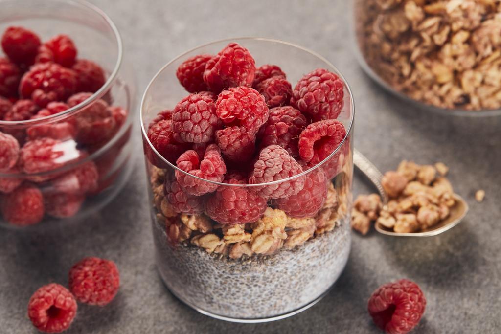 selective focus of tasty yogurt with raspberries, oat flakes and chia seeds near teaspoon on marble surface - Photo, Image