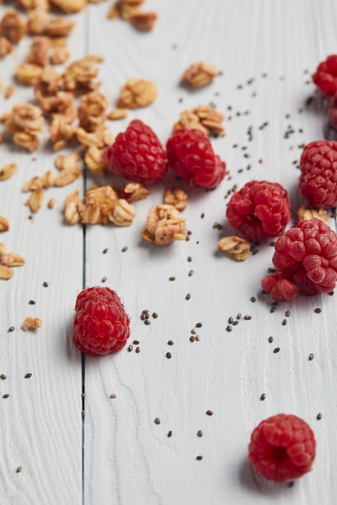selective focus of scattered raspberries, chia seeds and oat flakes on white wooden table - Photo, Image