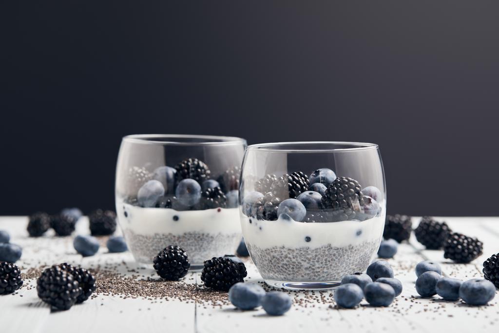 foyer sélectif de yaourt avec des graines de chia et des baies dans des verres près de graines éparses, myrtilles et mûres sur la table blanche isolé sur noir
 - Photo, image