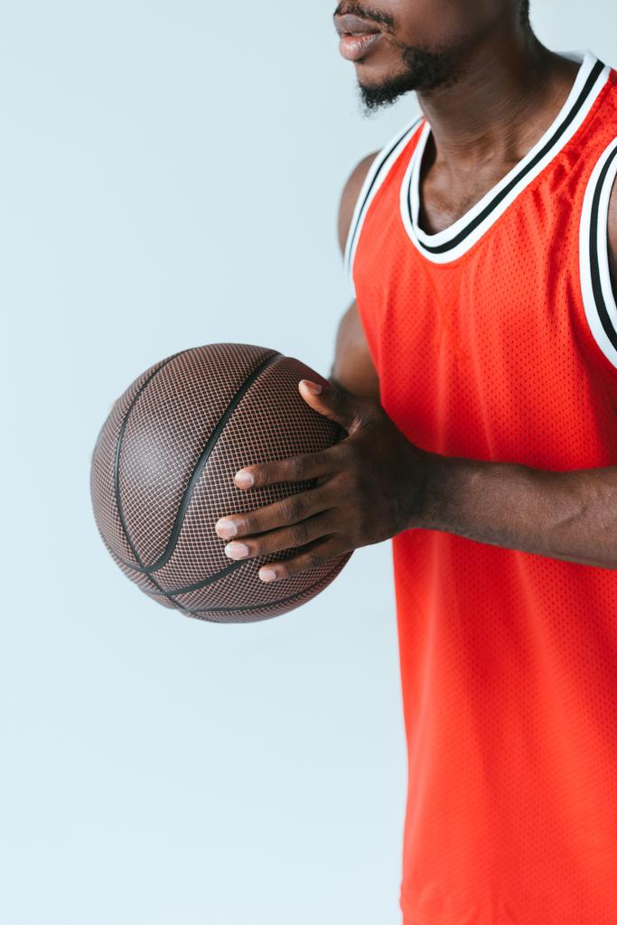 灰色で隔離されたボールを保持するアフリカ系アメリカ人バスケットボール選手のトリミングされたビュー - 写真・画像