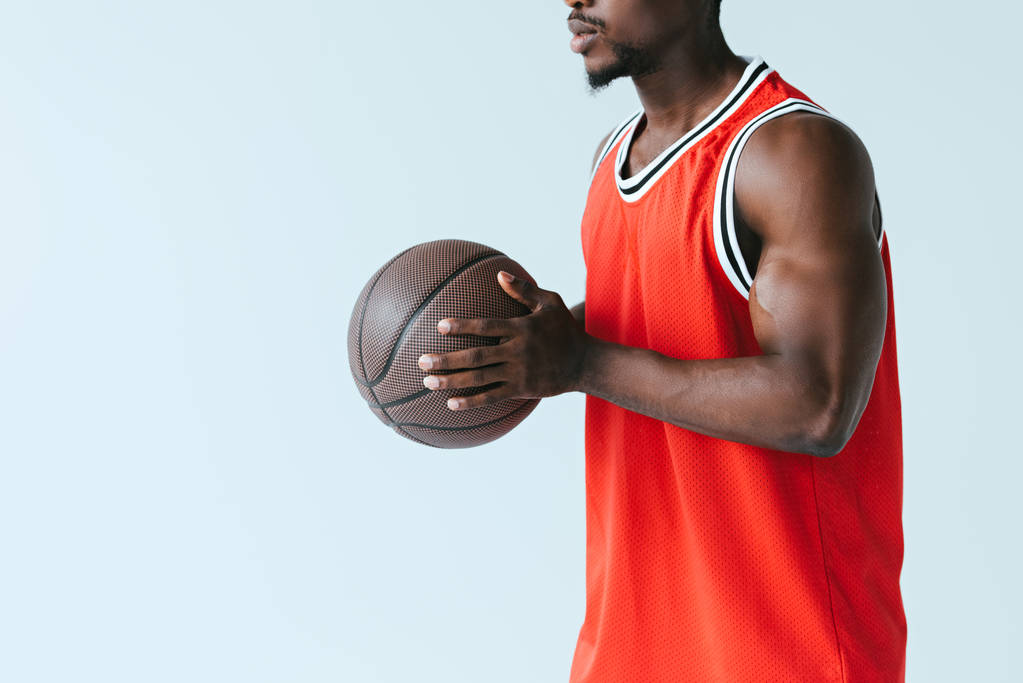 灰色で隔離されたバスケットボールボールを保持するアフリカ系アメリカ人スポーツマンのトリミングされたビュー - 写真・画像