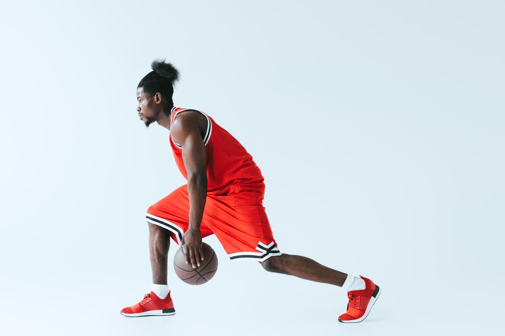 灰色の背景にバスケットボールをする赤いスポーツウェアのアフリカ系アメリカ人スポーツマン - 写真・画像