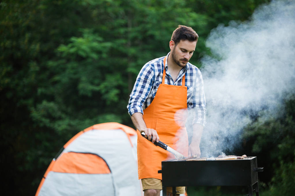 Handsome young male preparing barbecue outdoors for friends - Photo, Image