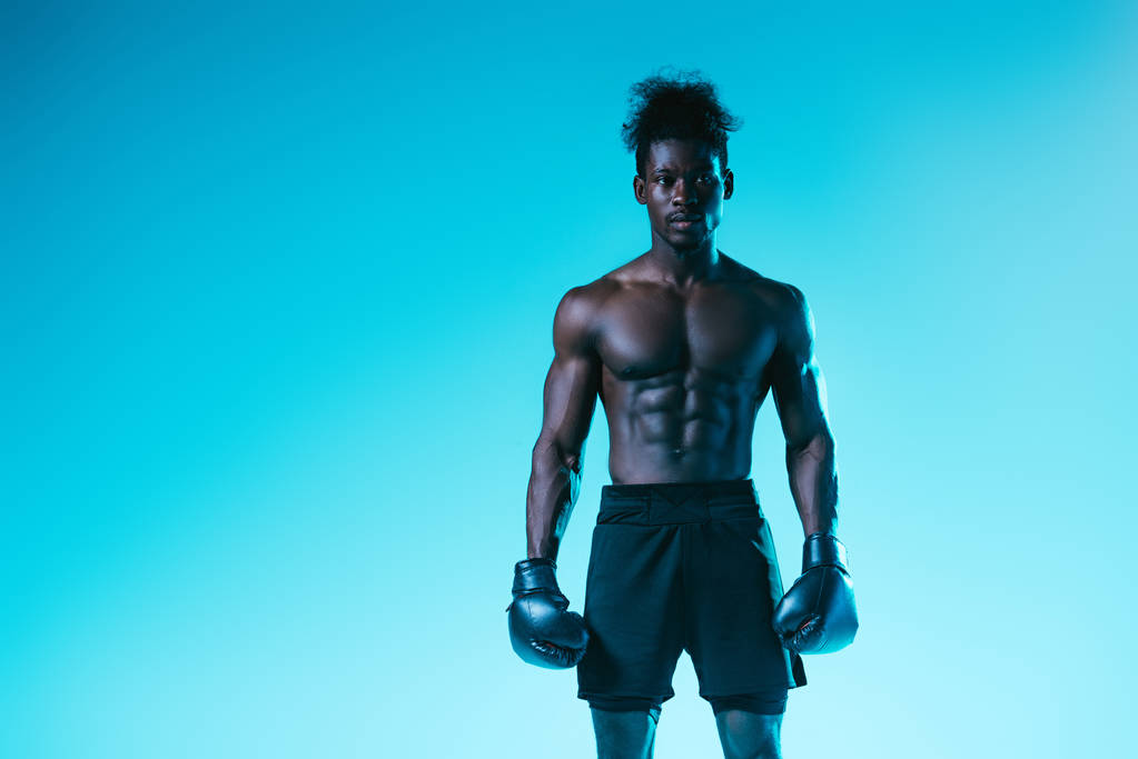 confident african american boxer with muscular torso looking at camera on blue background - Photo, Image