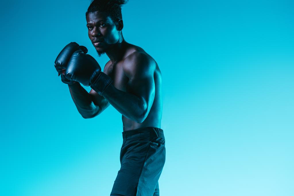 shirtless, gespierde African American sportman Boksen op blauwe achtergrond - Foto, afbeelding