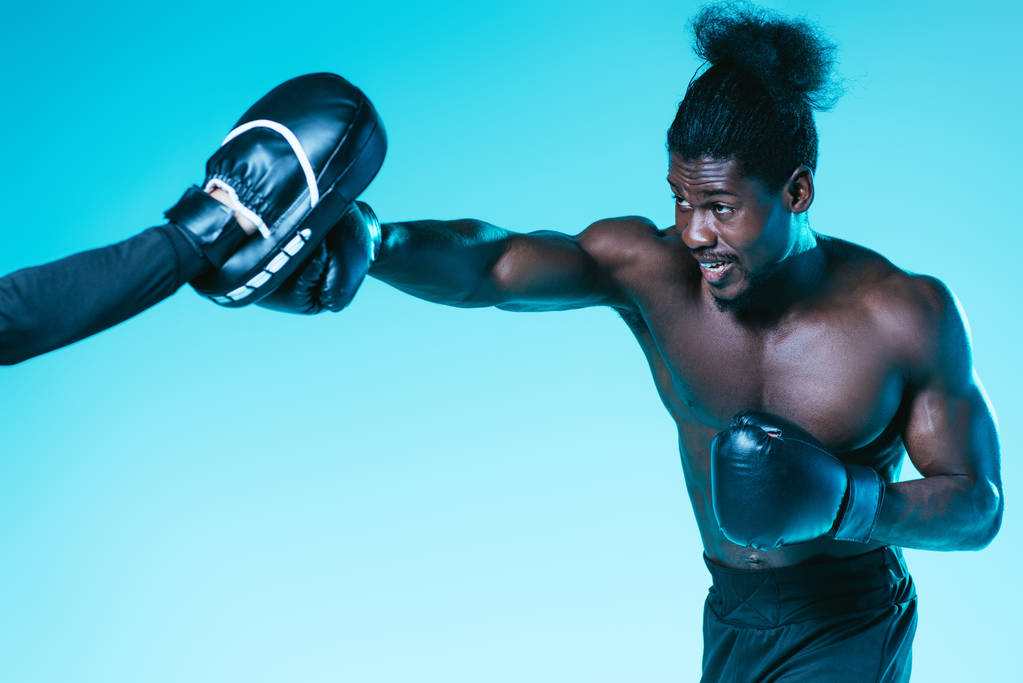 Afrikanischer Boxer trainiert mit Trainer auf blauem Hintergrund - Foto, Bild