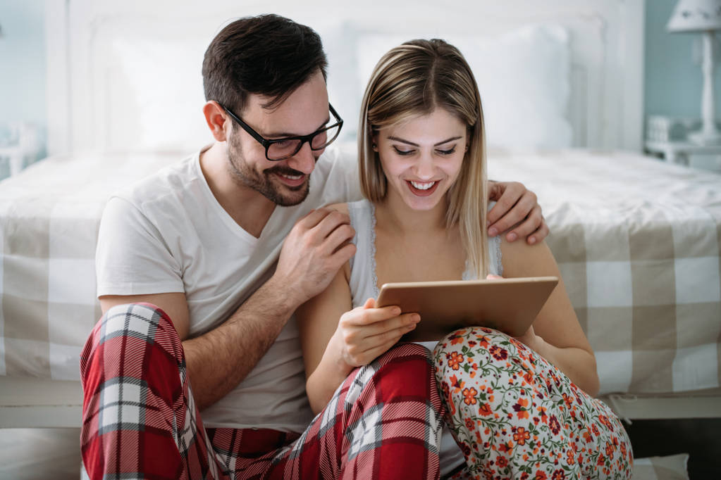 Giovane coppia felice utilizzando tablet digitale in camera da letto
 - Foto, immagini