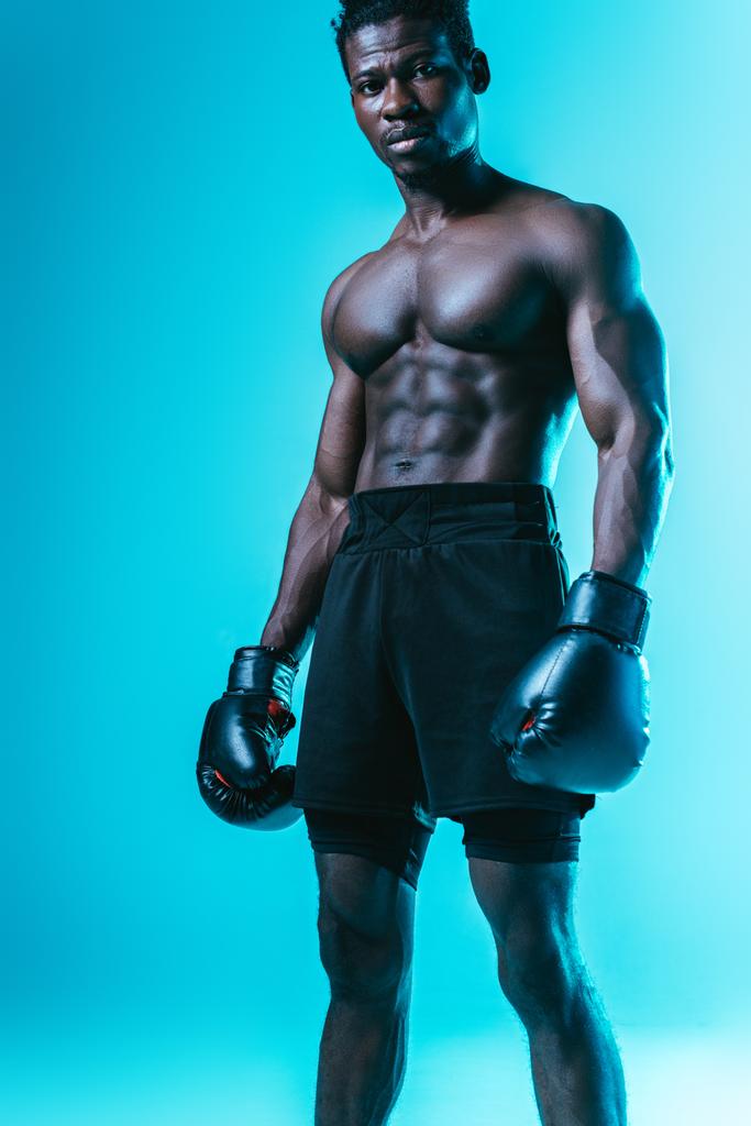 poważny, muskularny African amerykański bokser patrząc na aparat na niebieskim tle - Zdjęcie, obraz