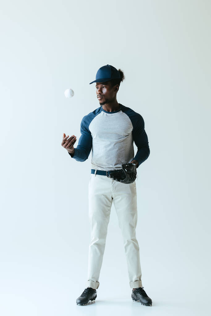 knappe Afro-Amerikaanse sportman in honkbal handschoen spelen met bal op grijze achtergrond - Foto, afbeelding