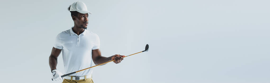 πανοραμικό σφηνάκι του όμορφου αφρικανικού Αμερικάνικου αθλητή που κρατά το γκολφ κλαμπ απομονωμένο σε γκρι - Φωτογραφία, εικόνα