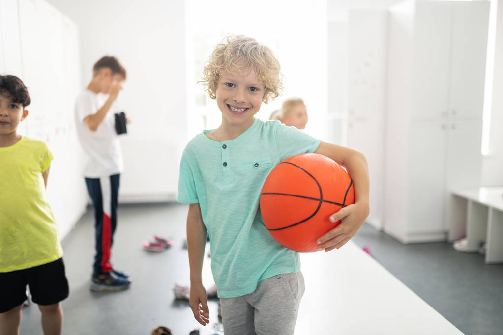 Aluno sorridente segurando basquete no vestiário
. - Foto, Imagem