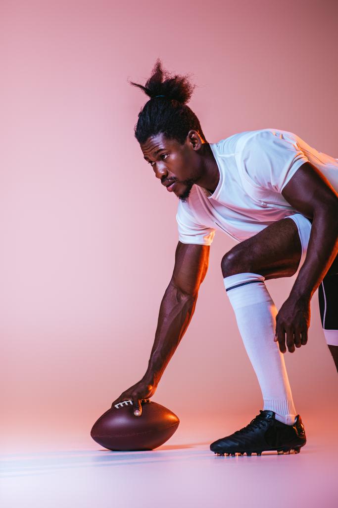 молодой африканский американский спортсмен играет в американский футбол на розовом фоне с градиентом и освещением
 - Фото, изображение