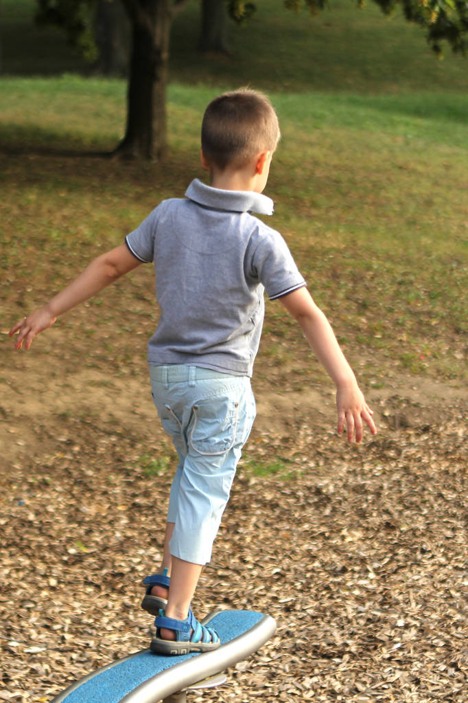 poika esikoululainen shortseissa kävelee vaakasuorassa urheilupeli ammus leikkikentällä puistossa kesällä, koulutuksen koordinointi ja kehon tasapaino
 - Valokuva, kuva