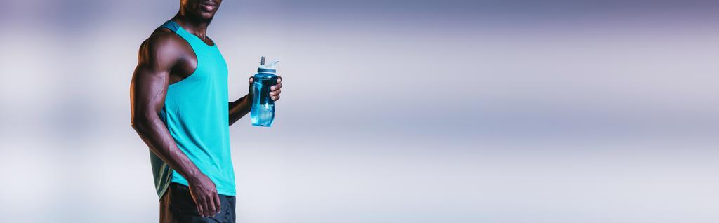 vista recortada del deportista afroamericano sosteniendo botella deportiva sobre fondo gris con iluminación, plano panorámico
 - Foto, imagen