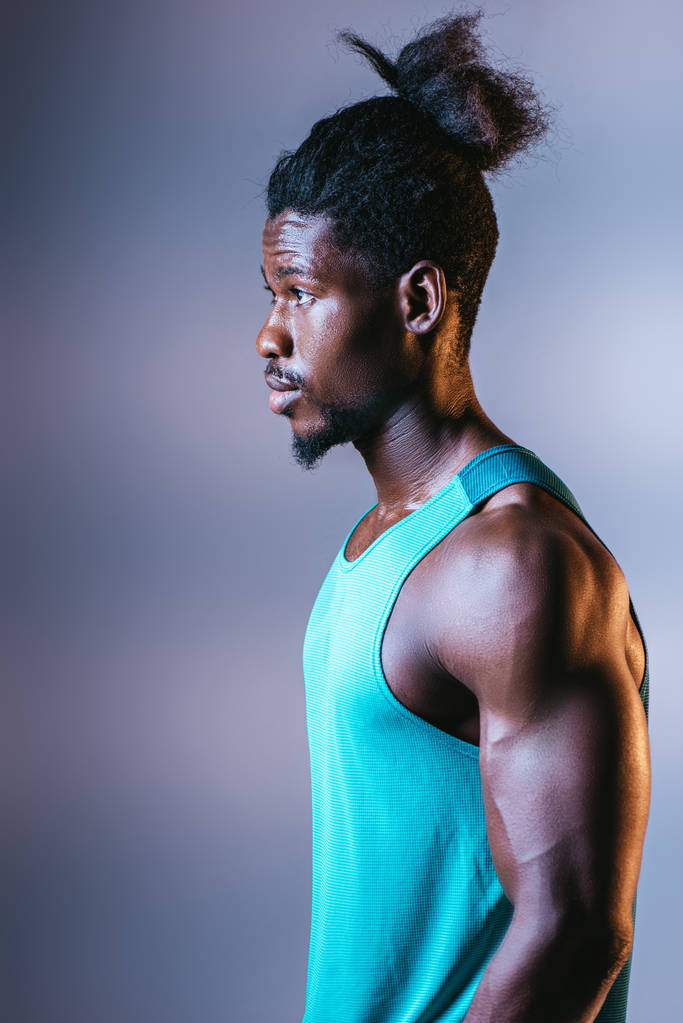 νεαρός, ένας Αφρικανός Αμερικανός αθλητής που κοιτάζει μακριά σε γκρίζο φόντο με φωτισμό - Φωτογραφία, εικόνα